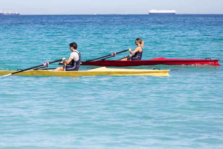 Coastal Rowing ist Teamplay! Zwei Ruderer in gelben und roten Coastal Booten (X-Adventure) rudern im türkisfarbenen Wasser.